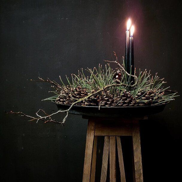 a candle that is sitting on top of a wooden stand with pine cones and branches