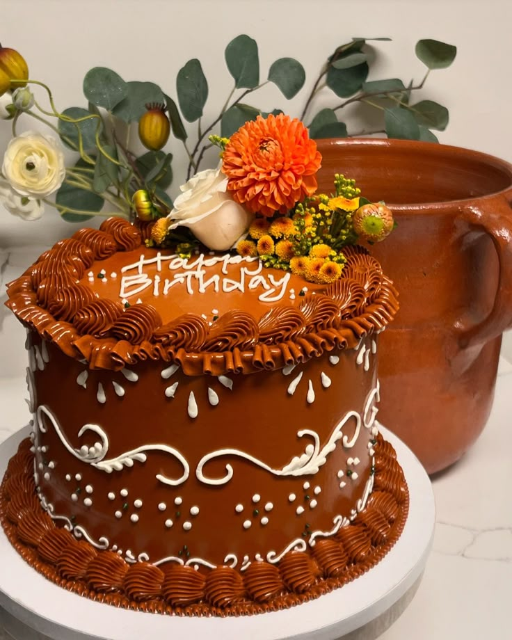 a chocolate birthday cake sitting on top of a white plate next to a potted plant