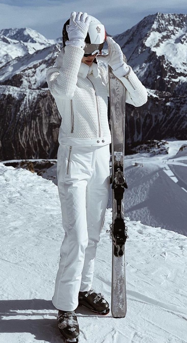 a man holding a snowboard on top of a snowy mountain covered in snow with mountains in the background