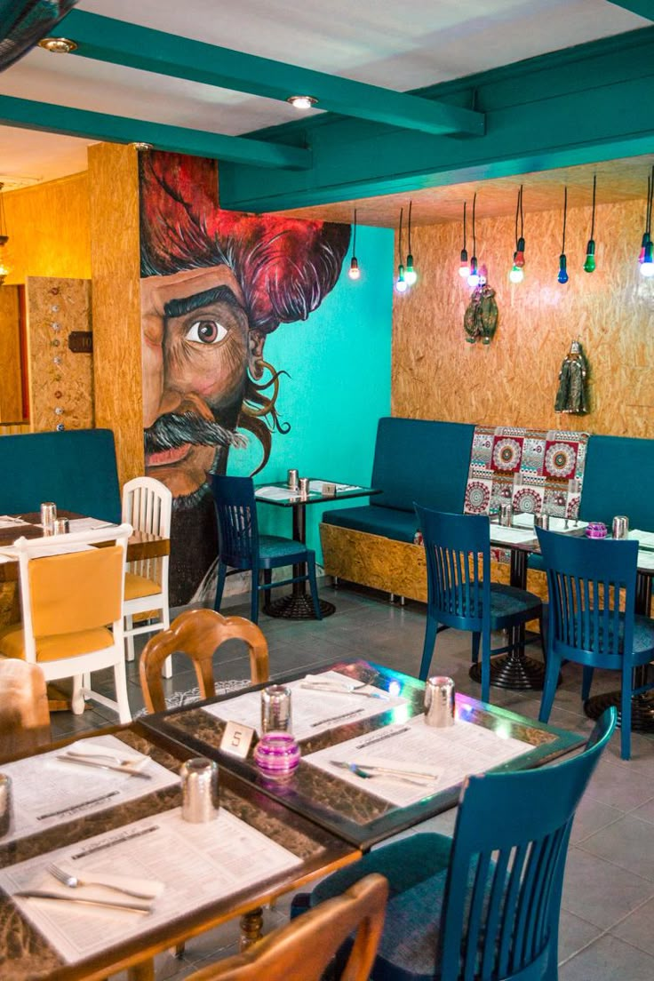 the interior of a restaurant with blue chairs and tables, painted mural on the wall