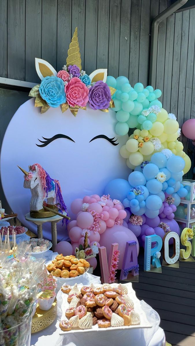 a table topped with lots of desserts next to a giant unicorn head balloon wall