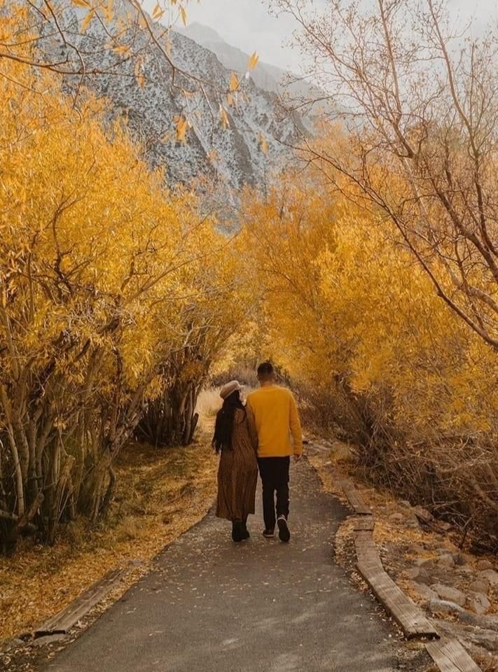 a man and woman walking down a path in the woods with yellow trees around them