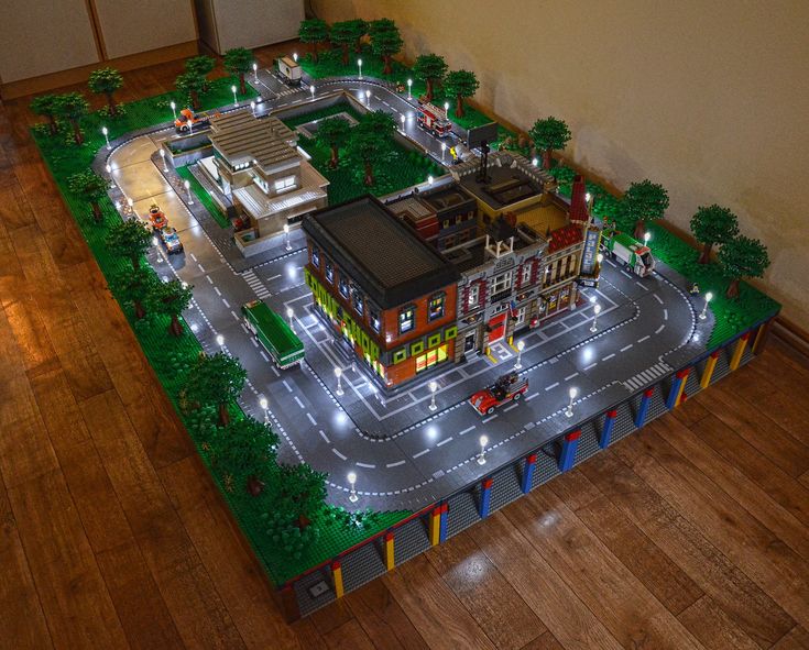 a model of a city with cars and buildings on the street at night, in front of a wall