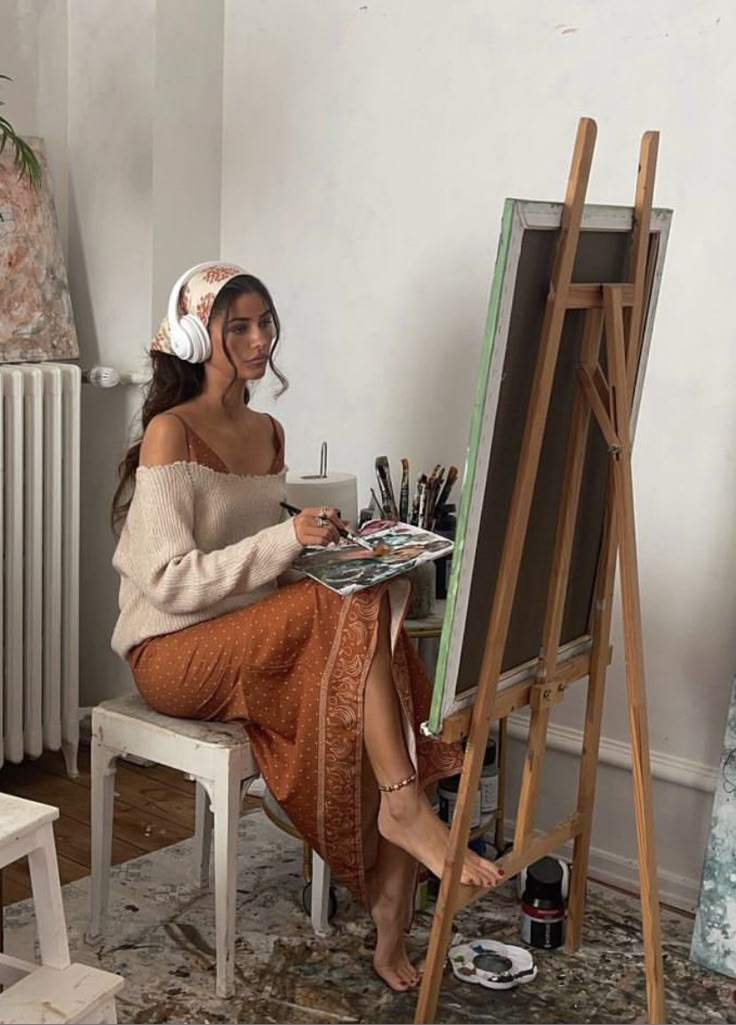 a woman is sitting in front of an easel with paint and brushes on it