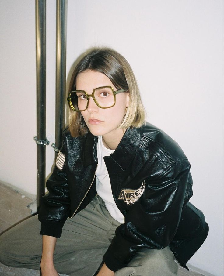 a woman with glasses sitting on the ground next to a pole and pipe holder in front of her