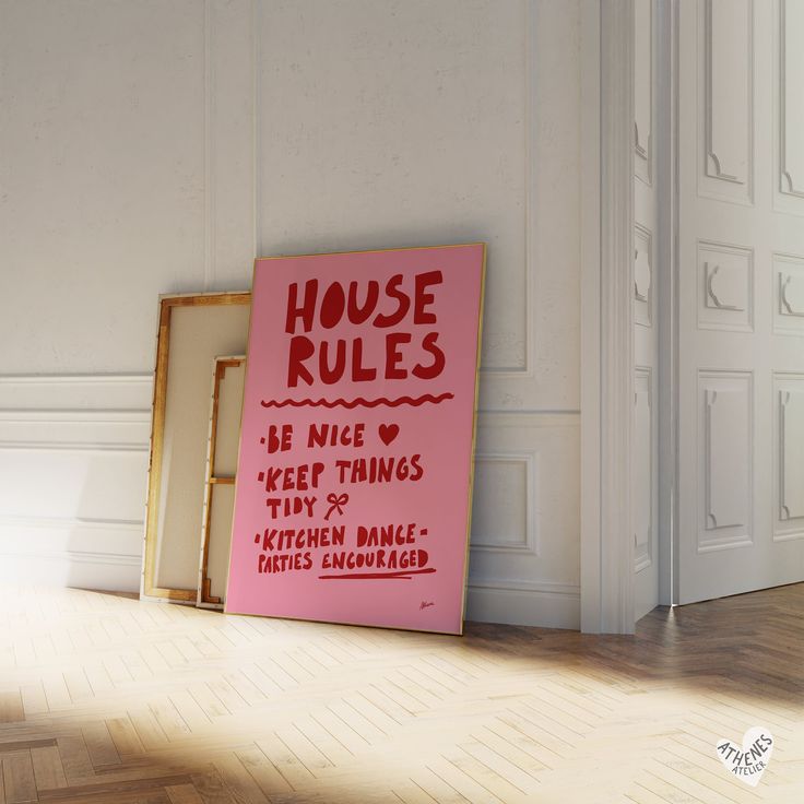 there is a pink sign on the floor next to two framed pictures that read house rules be nice keep things tidy