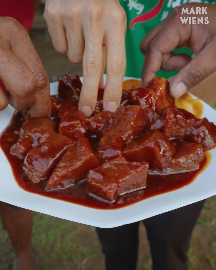 two hands reaching for some food on a white plate with red sauce in front of them