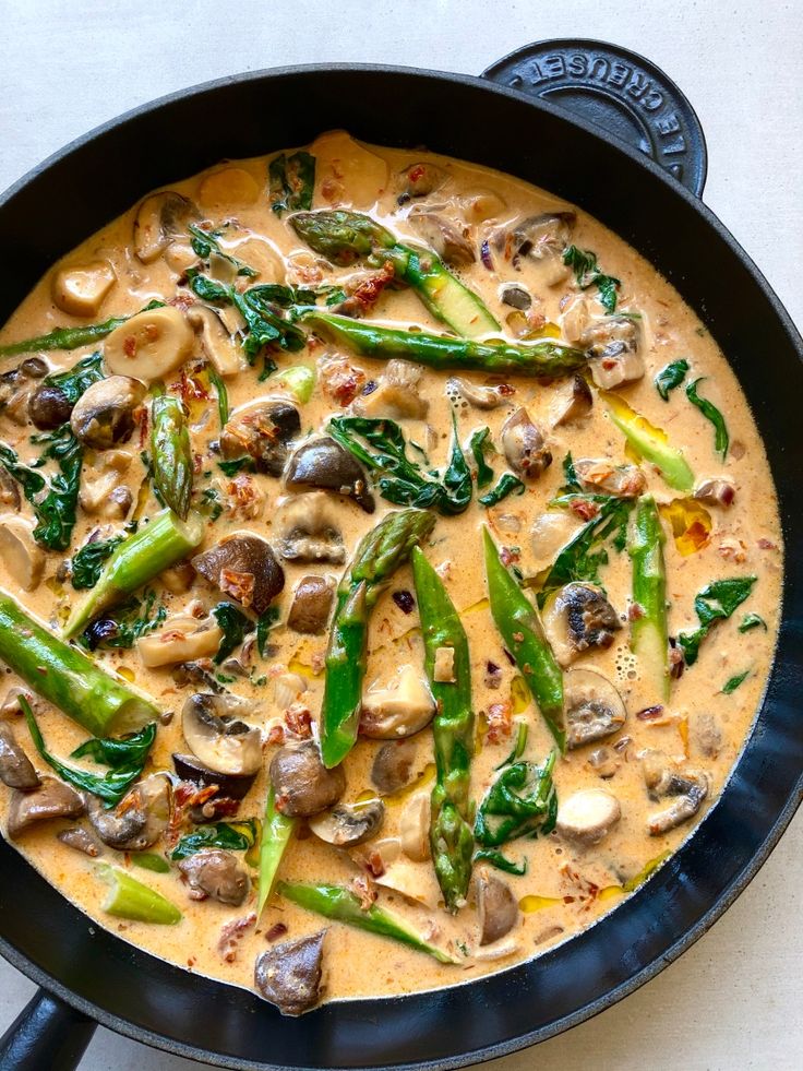 a skillet filled with mushrooms, asparagus and other vegetables on top of a table