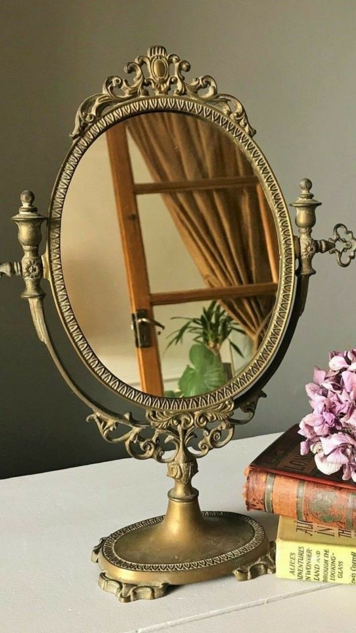 a mirror sitting on top of a table next to a pile of books and a pink flower