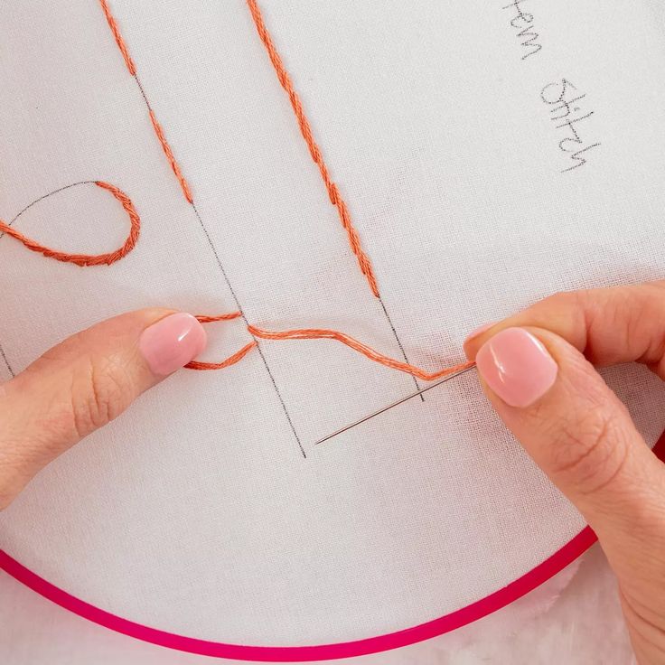 someone is stitching something on a piece of paper with orange thread and pink nail polish