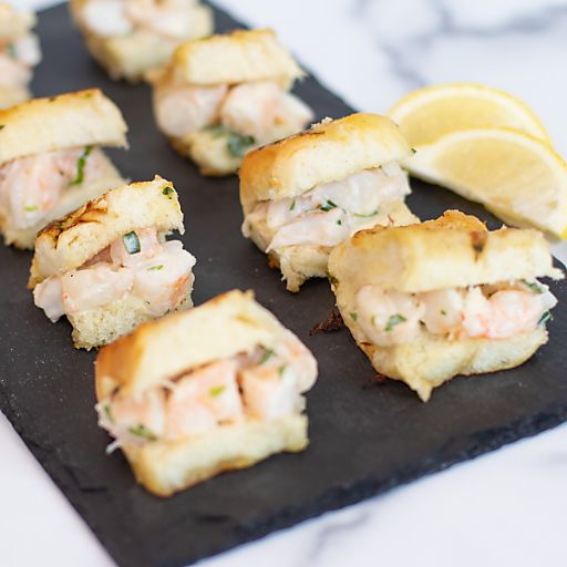 small sandwiches with shrimp and cheese on a black slate board next to lemon wedges