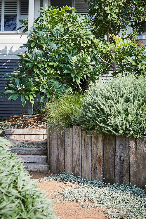 a wooden fence in front of a house with trees and bushes on the side walk