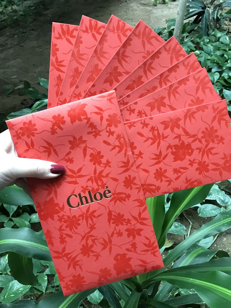 a person holding up four red envelopes with the word chloe on them in front of green plants