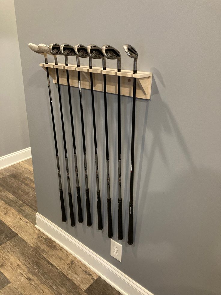 five golf clubs are hanging on the wall in a room with wood flooring and gray walls