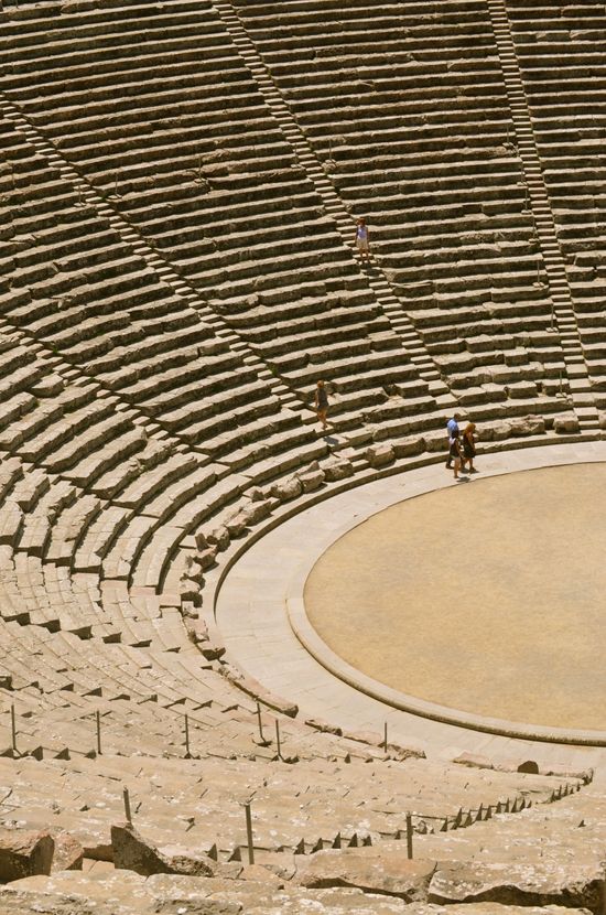 two people are standing in the middle of an empty amphite with stone seats