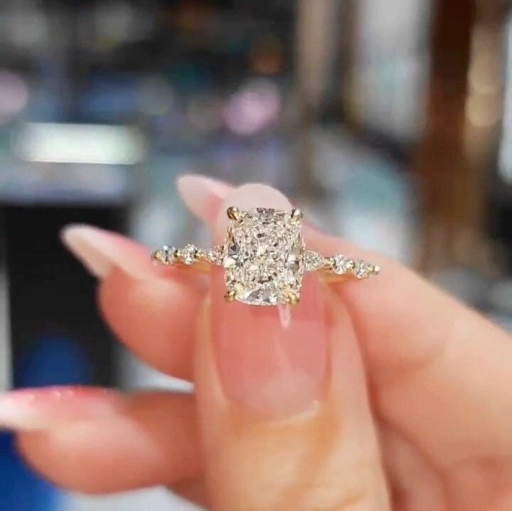 a woman's hand holding an engagement ring in front of her face, with the diamond