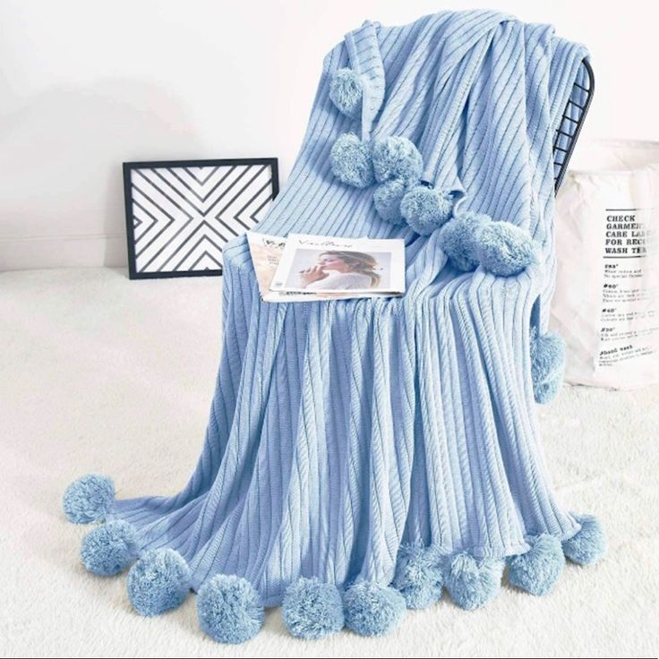 a blue blanket with pom poms on it sitting next to a white wall