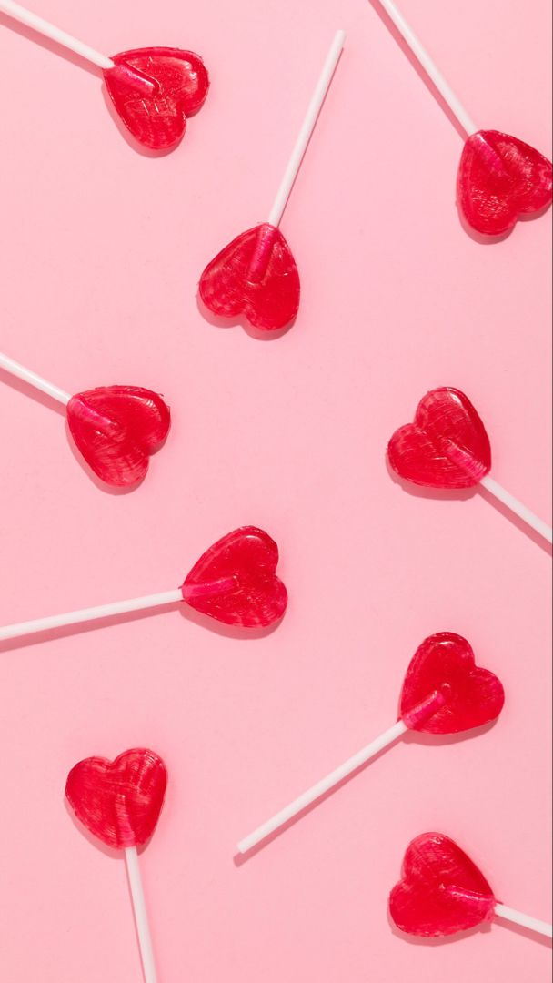 lollipops in the shape of hearts are on a pink surface with white sticks