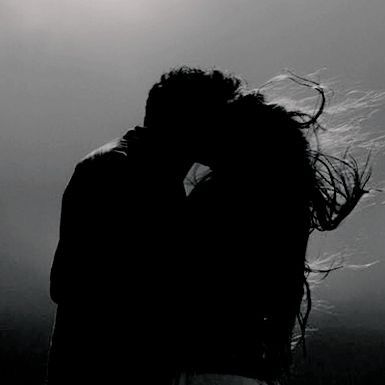 a man and woman kissing in the dark under some light from behind them, with their hair blowing in the wind