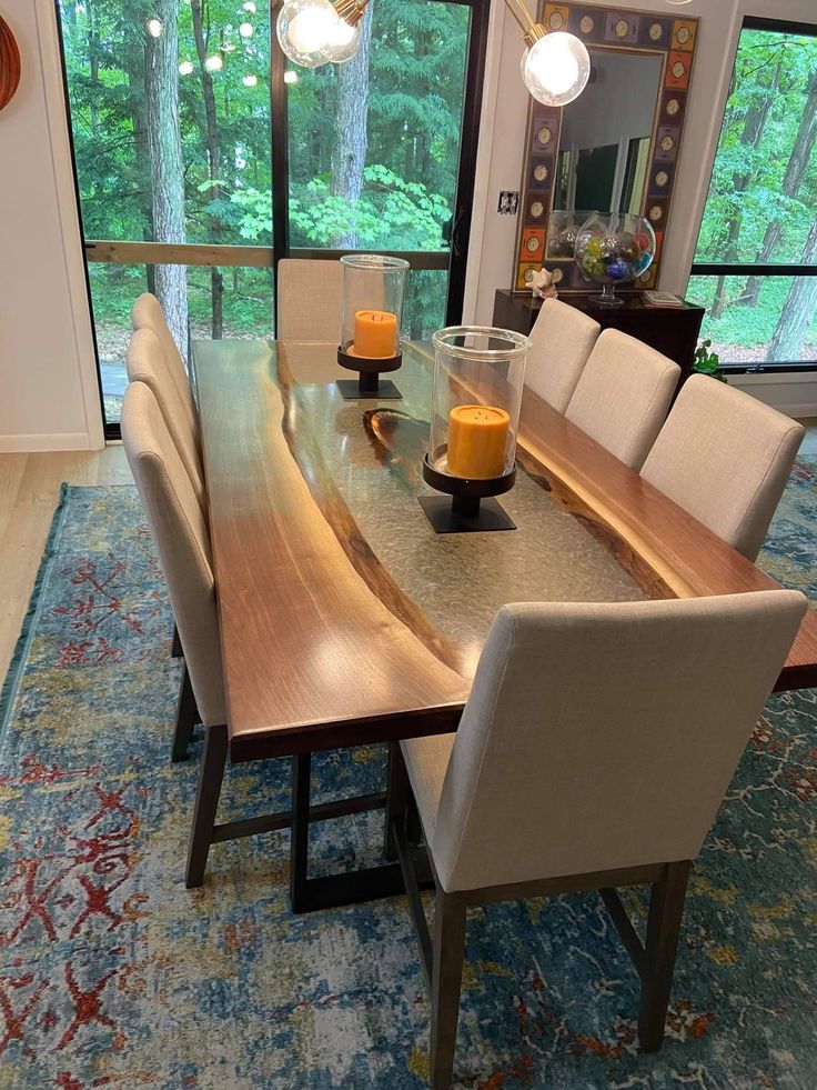 a dining room table with chairs and a vase on the centerpiece, in front of a large window