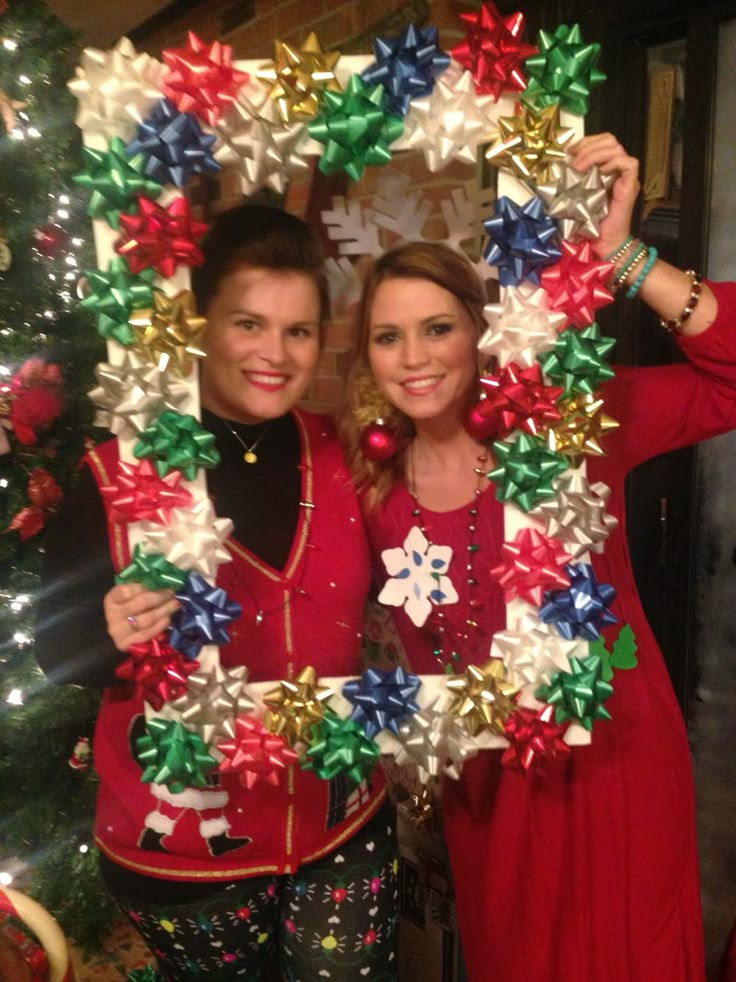 two people standing next to each other in front of a christmas wreath with bows on it