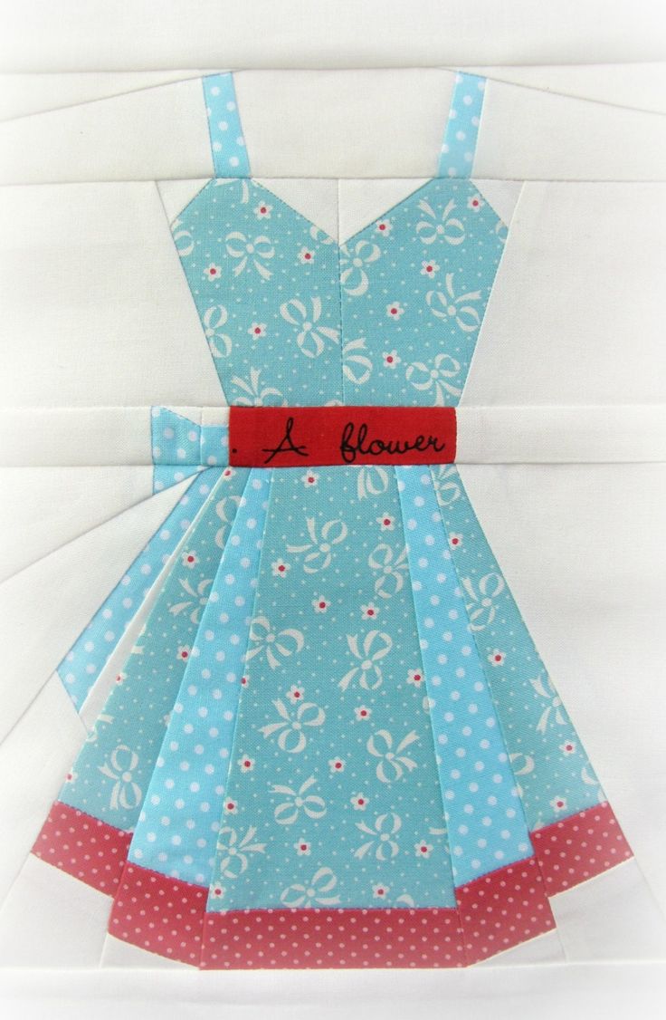 a blue dress with white and red polka dots on it, sitting on top of a quilt