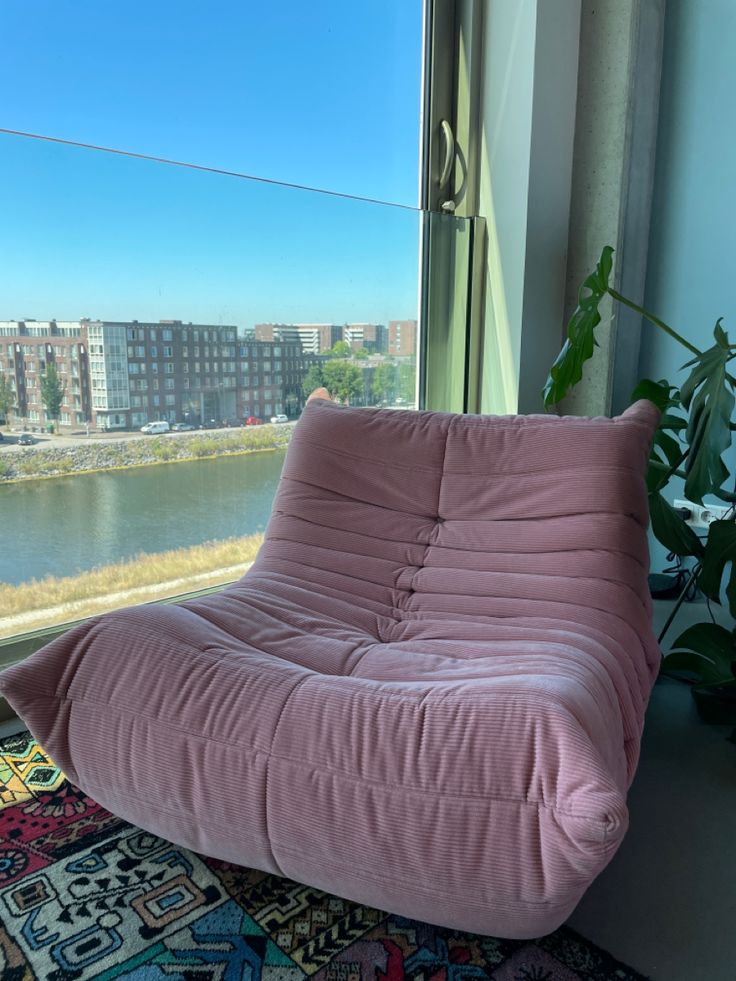 a pink bean bag chair sitting on top of a rug next to a large window