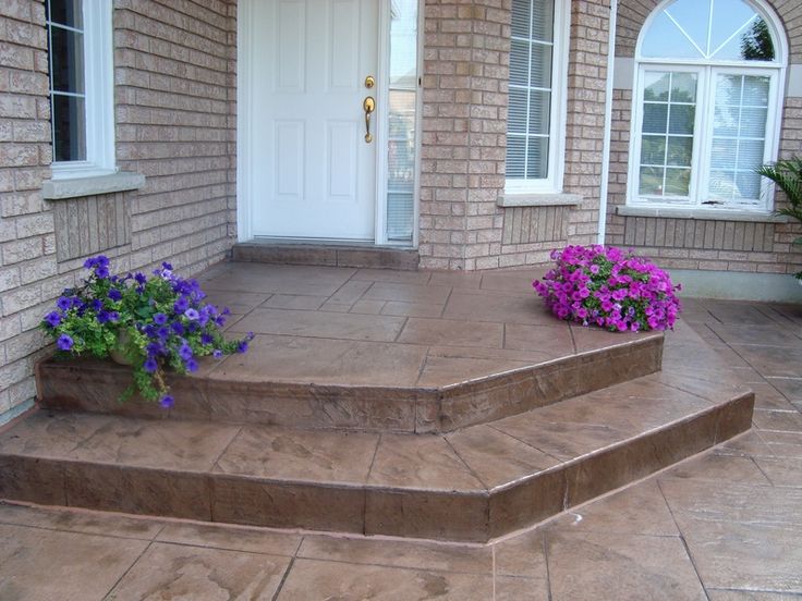 some purple flowers are sitting on the steps in front of a brick house with white doors and windows