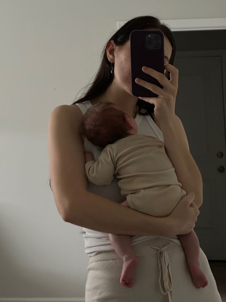 a woman holding a baby in her arms and taking a photo with her cell phone