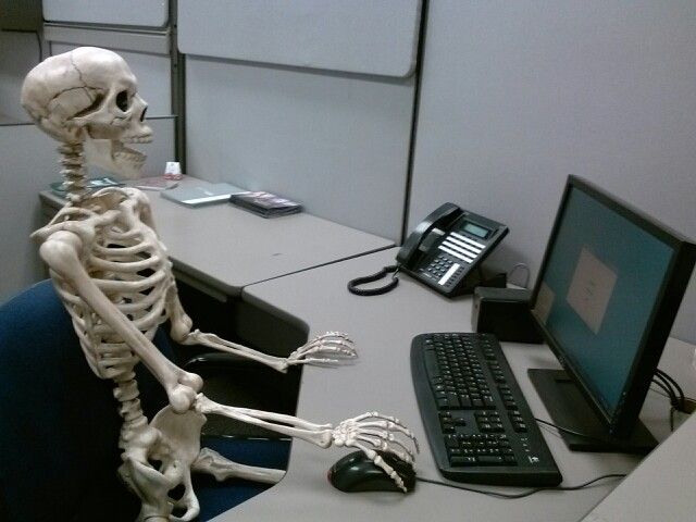 a skeleton sitting in front of a computer on a desk