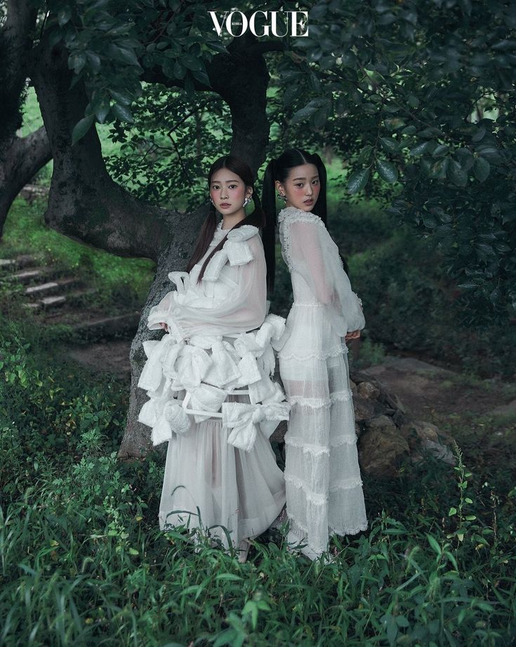 two women in white dresses standing next to each other on the cover of a magazine