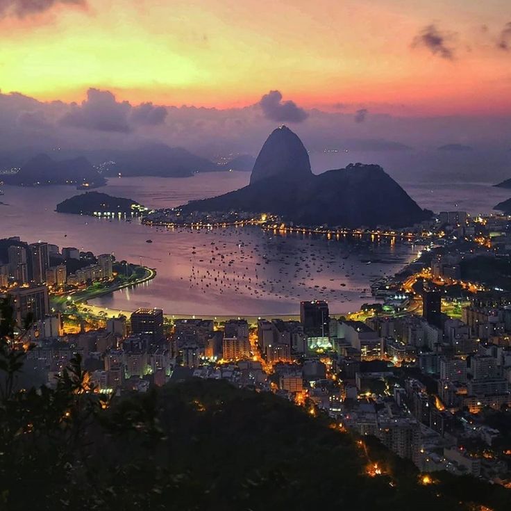 an aerial view of the city lights and water at night with mountains in the background