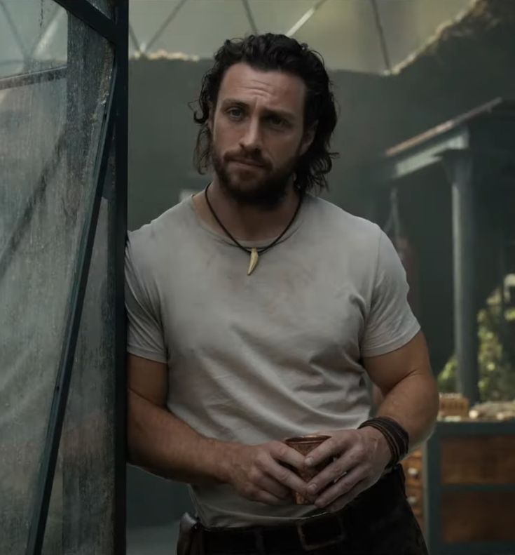 a man with long hair and beard standing in front of a glass door wearing a cross necklace