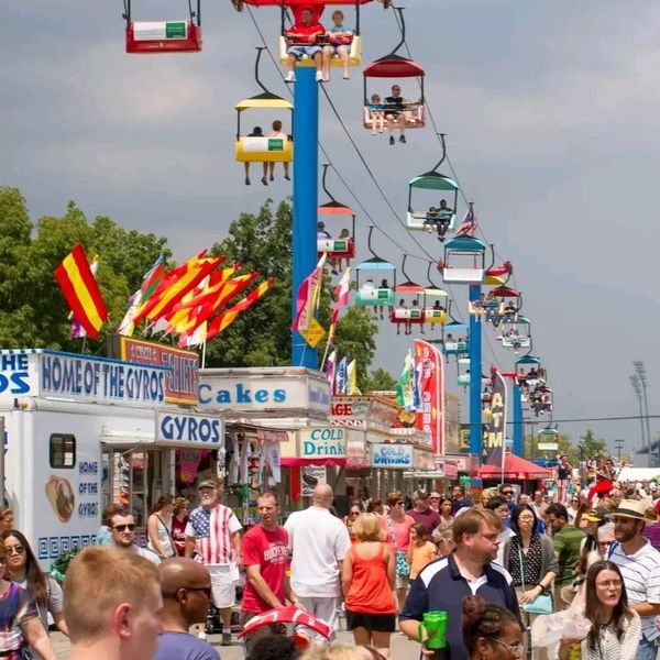 a crowd of people walking down a street next to food trucks and carnival rides in the background