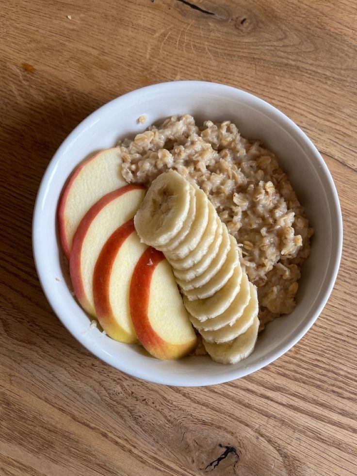 a bowl filled with oatmeal, apples and sliced bananas on top of a wooden table