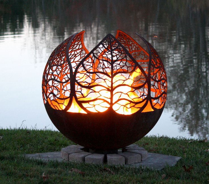 a fire pit sitting on top of a lush green field next to a lake in the evening