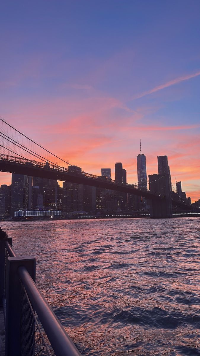 the sun is setting over the city skyline as it reflects in the water and bridge