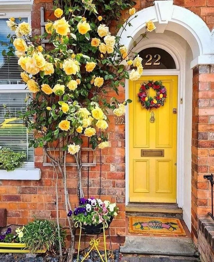 a yellow front door with wreath and flowers on it