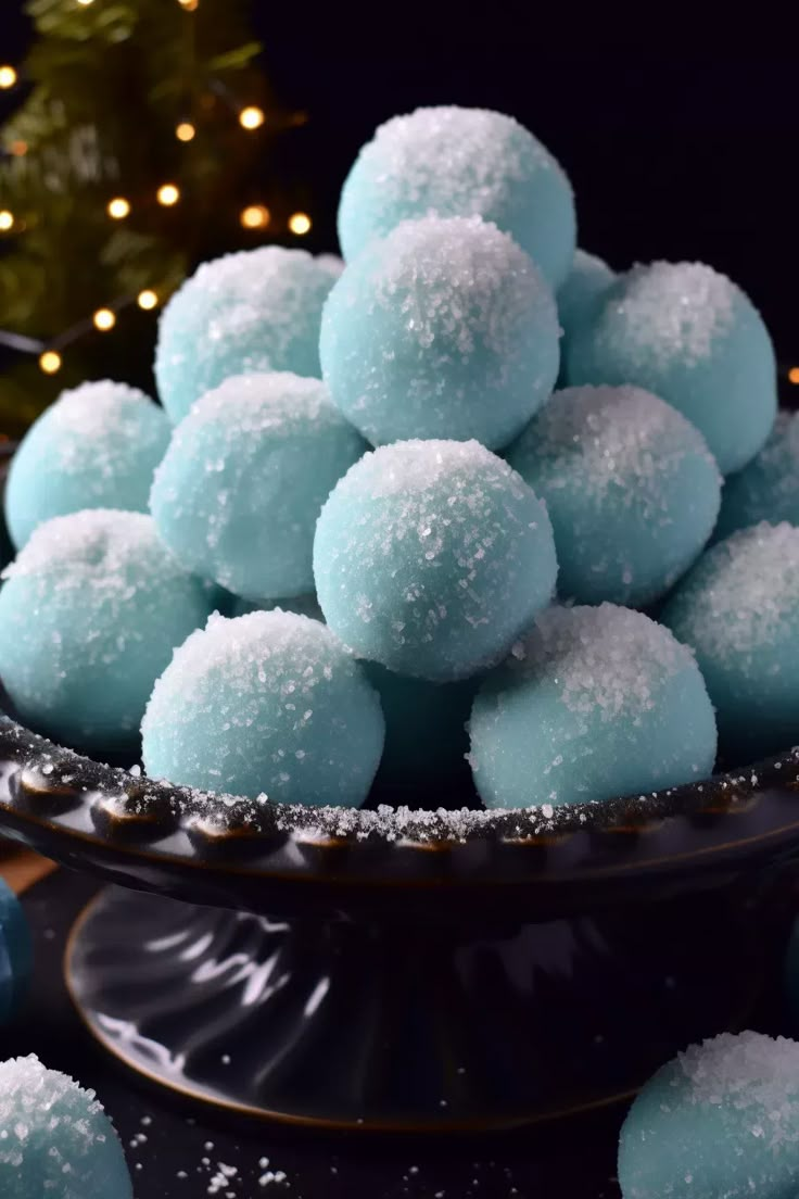 a bowl filled with sugar covered donuts next to a christmas tree