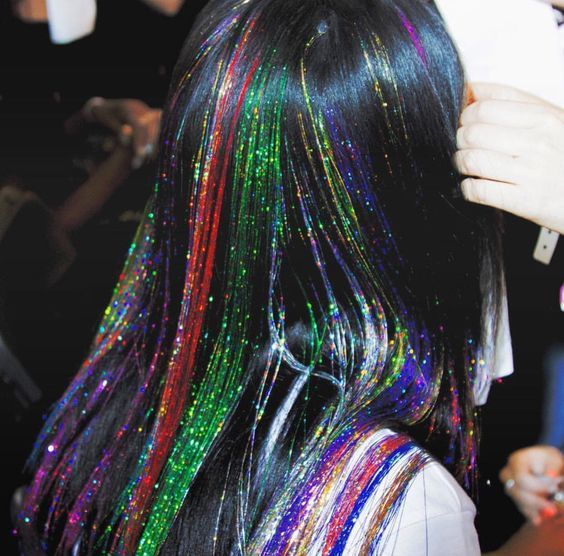 a woman with long black hair covered in multicolored glitters is getting her hair done