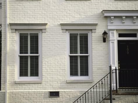 a white brick building with two windows and a black gate on the front door is shown