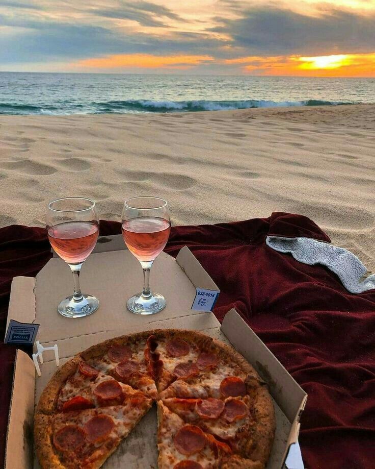 two glasses of wine and a pizza on the beach