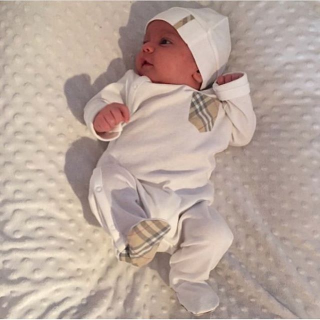 a baby laying on top of a bed wearing a white hat and bow tie shirt