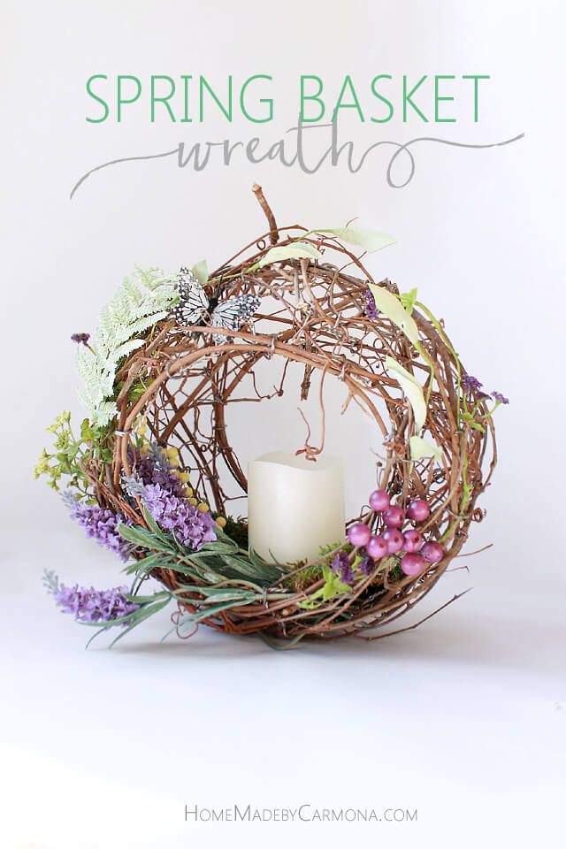 a white candle sitting inside of a wreath with purple flowers and greenery around it