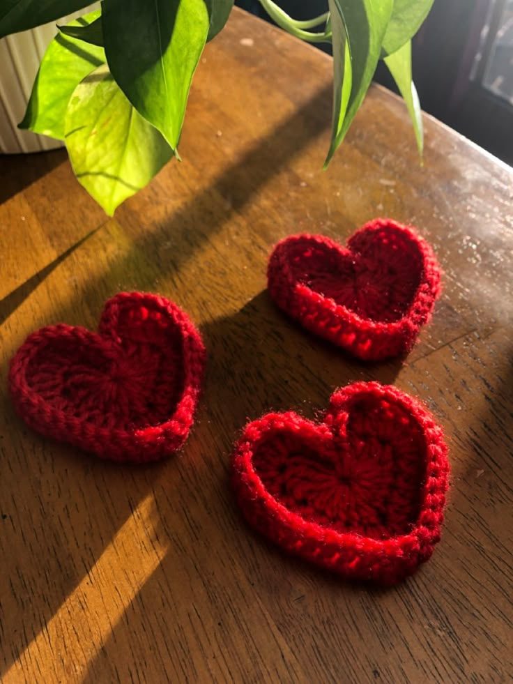 three crocheted hearts sitting on top of a wooden table next to a potted plant