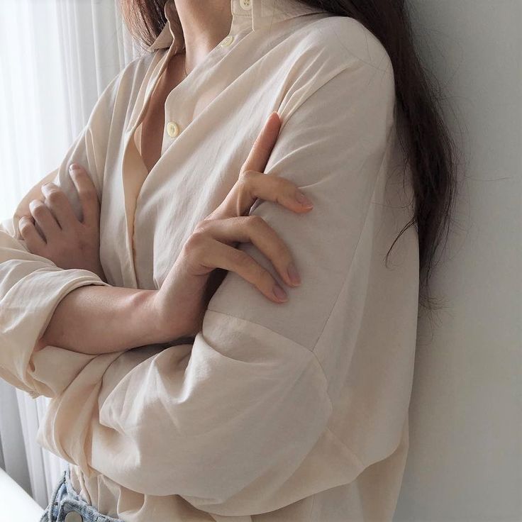 a woman with her arms crossed leaning against a wall and looking at the camera while standing in front of a window