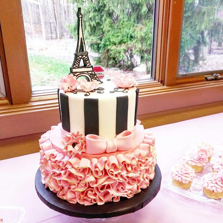 a pink and black cake sitting on top of a table next to cupcakes