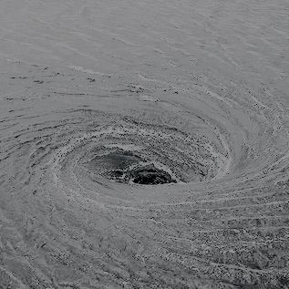 a black and white photo of a circular hole in the sand