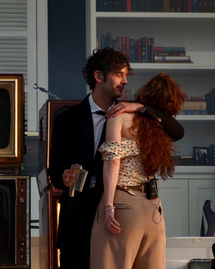 a man and woman standing next to each other in front of a book shelf with books on it