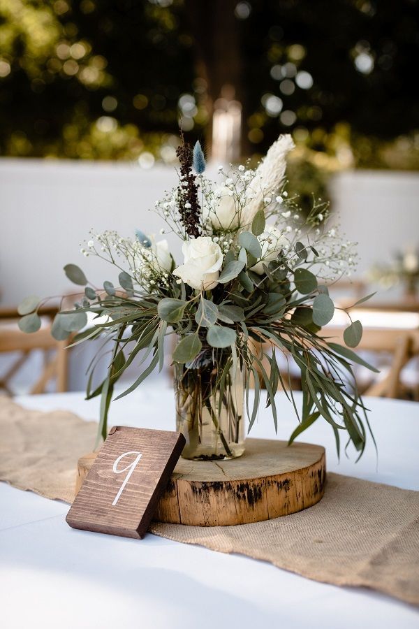 a wooden table topped with a vase filled with white flowers and greenery next to a number one sign